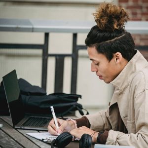 young serious ethnic man with trendy hairstyle writing at table